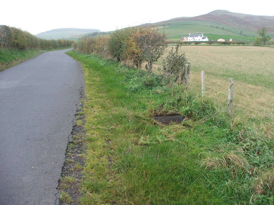 Looking south along the Bowmont Valley. Cliftoncote is in the distance and the fallen milestone partially uncovered at the gap in the hedgerow